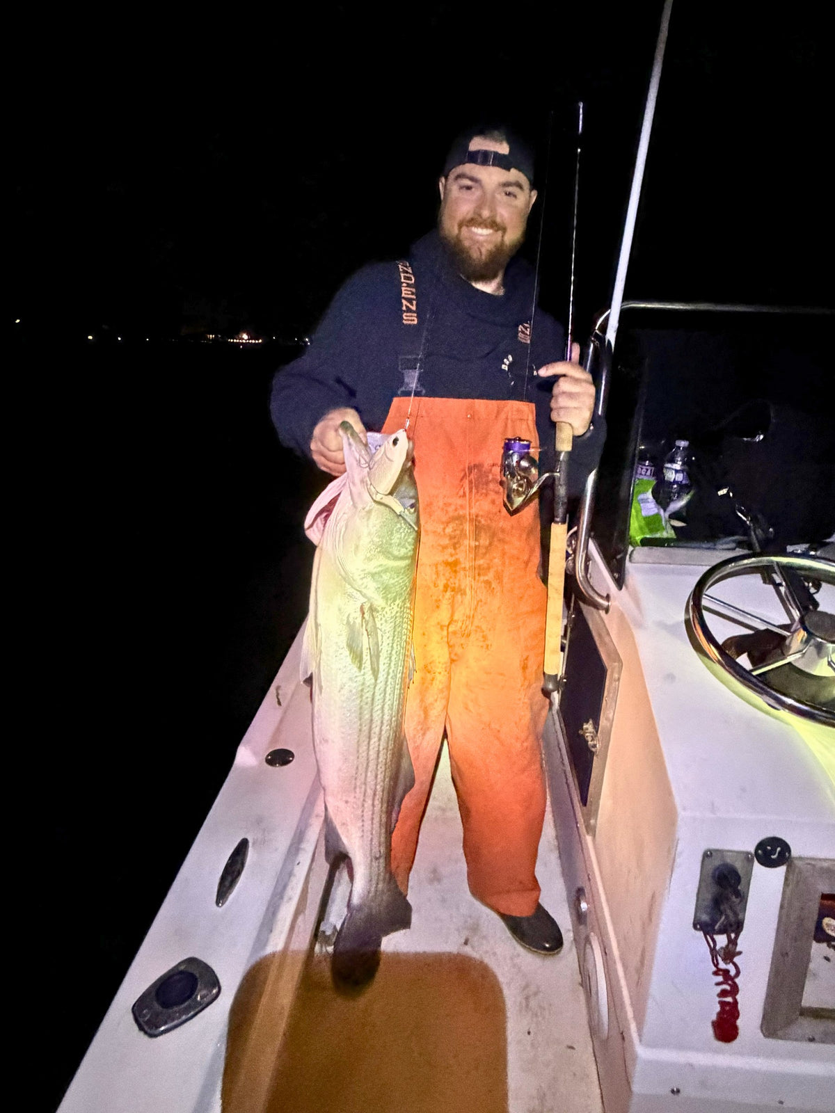 Angler in orange bibs with a striped bass and Inshore Reaper rod at night