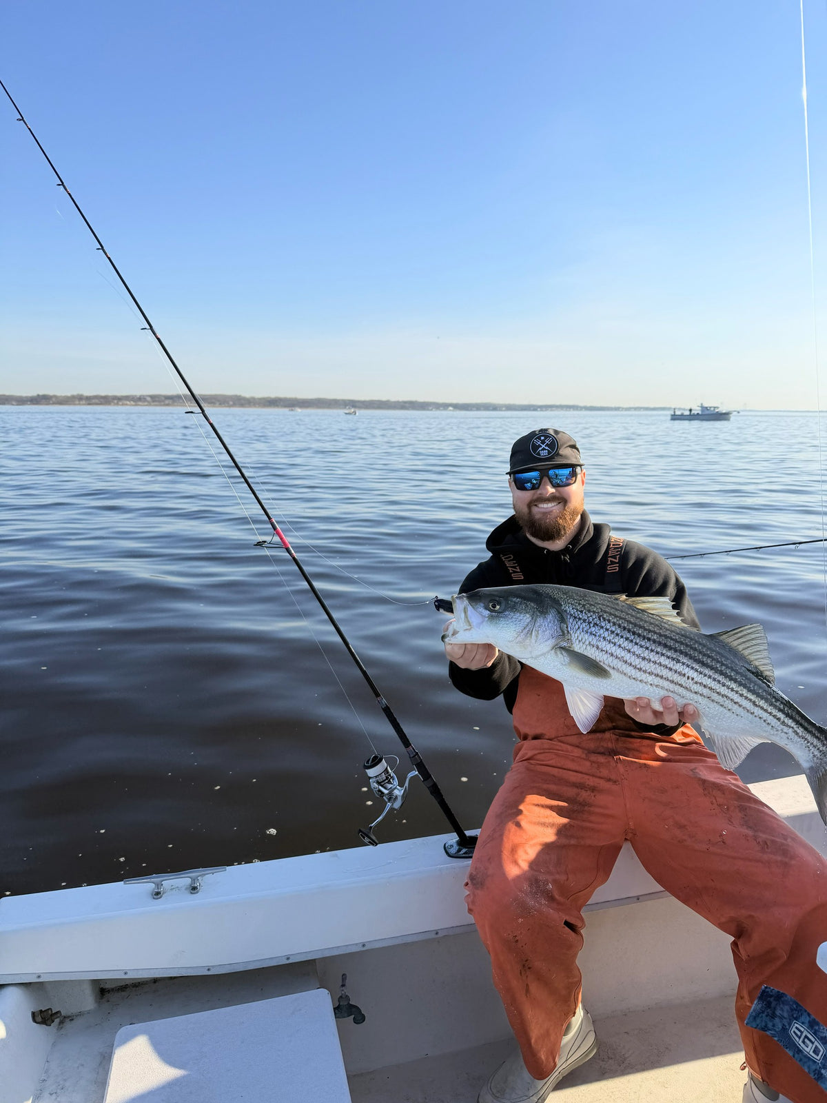 Angler in orange bibs with a striped bass caught on a Tiderunner rod