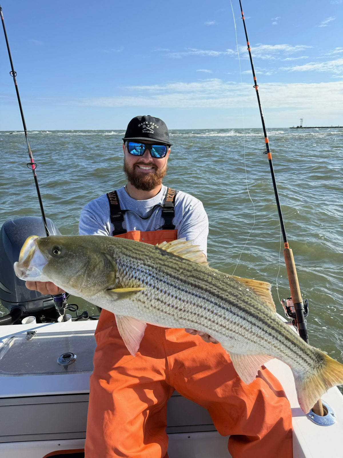 Angler in bibs holding a striped bass, Tiderunner rod in the holder